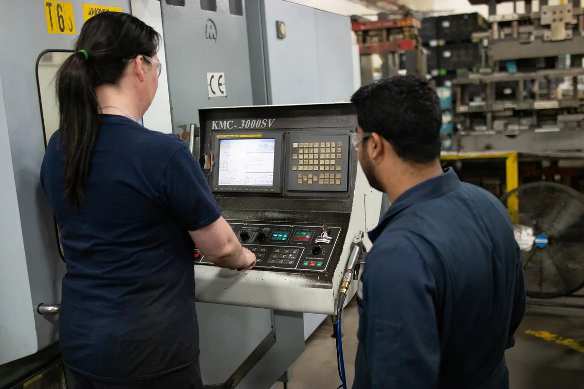 Two Clover team members working together at a CNC lathe.